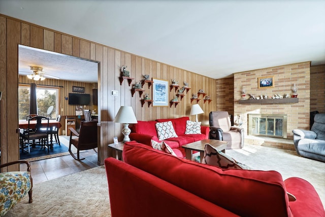 living area featuring wooden walls, ceiling fan, tile patterned flooring, and a fireplace