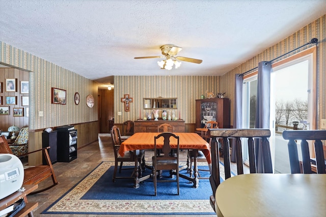 dining space featuring a wainscoted wall, a ceiling fan, wallpapered walls, and a textured ceiling