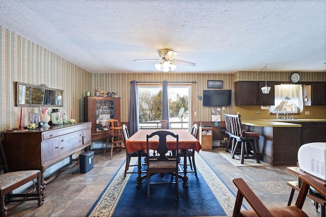 dining room with baseboard heating, stone finish floor, wallpapered walls, a textured ceiling, and a ceiling fan