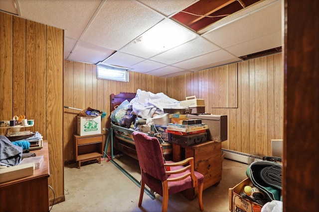 bedroom with a baseboard radiator, a paneled ceiling, wooden walls, and concrete floors