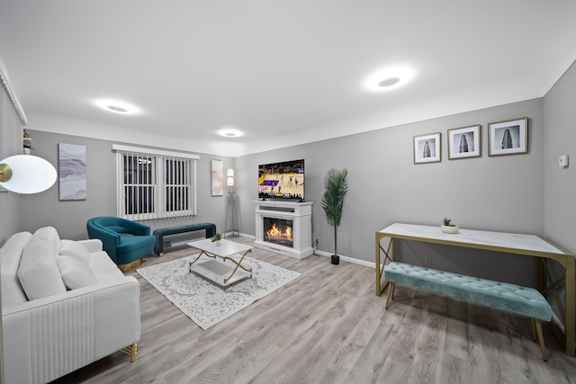 living area with baseboards, light wood-style floors, and a glass covered fireplace