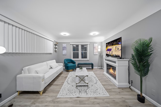 living room featuring light wood-style flooring, baseboards, and a glass covered fireplace