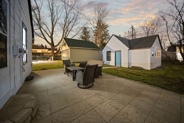 patio terrace at dusk with a lawn, an outdoor structure, and fence