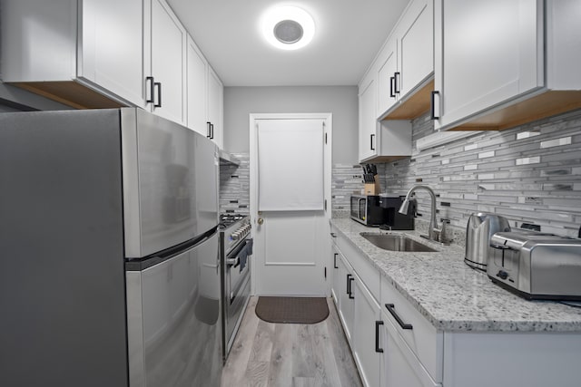 kitchen with light wood-style flooring, a sink, stainless steel appliances, white cabinets, and tasteful backsplash