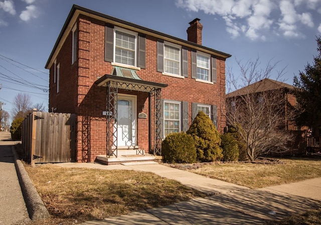 view of front of house with brick siding, a chimney, and fence