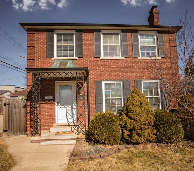 view of front facade with brick siding, a chimney, and fence