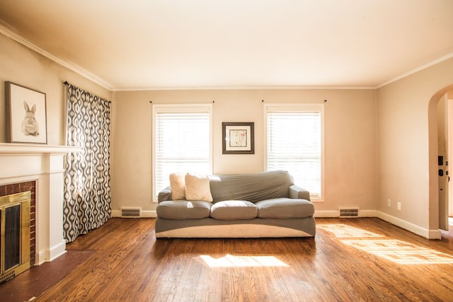 living area featuring visible vents, arched walkways, ornamental molding, hardwood / wood-style flooring, and a glass covered fireplace