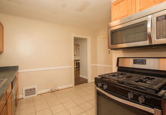 kitchen with light tile patterned floors, baseboards, visible vents, appliances with stainless steel finishes, and dark countertops