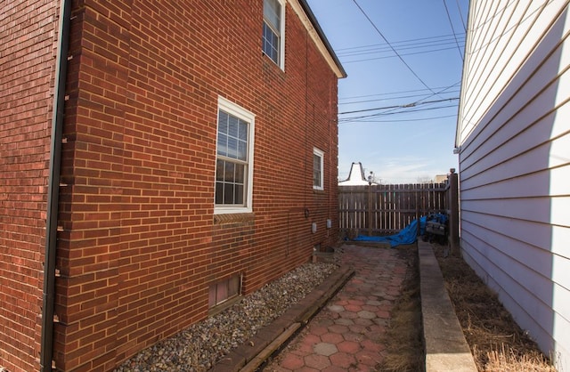 view of side of home featuring fence and brick siding