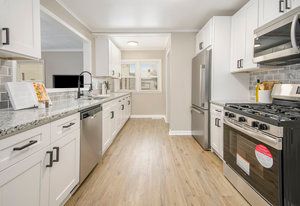 kitchen with light stone counters, light wood finished floors, white cabinets, appliances with stainless steel finishes, and tasteful backsplash