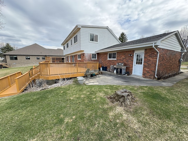 rear view of property with brick siding, a wooden deck, a yard, and a patio area