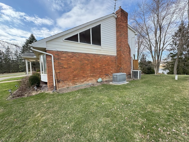 view of side of property with brick siding, a chimney, cooling unit, and a yard