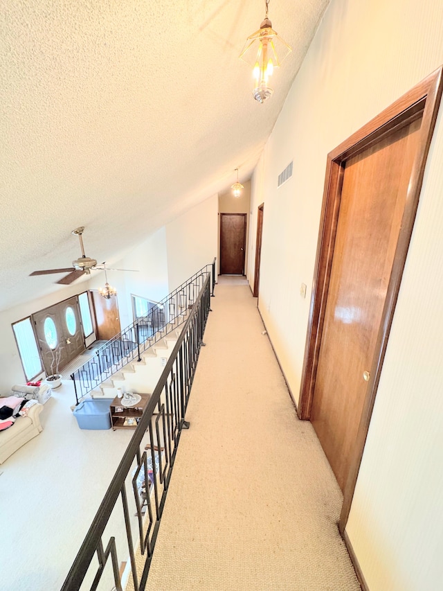 hall with light colored carpet, vaulted ceiling, visible vents, and a textured ceiling