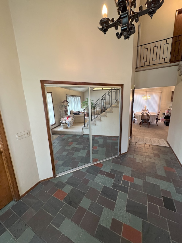 hallway featuring stairs, a towering ceiling, stone tile flooring, and a chandelier