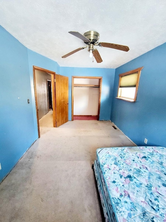 unfurnished bedroom featuring visible vents, ceiling fan, light carpet, a closet, and a textured ceiling