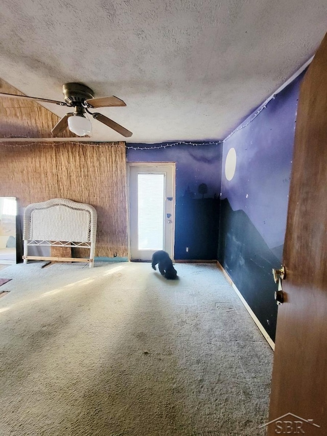 unfurnished bedroom featuring a ceiling fan, baseboards, carpet floors, wood walls, and a textured ceiling