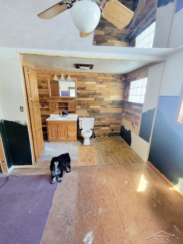 interior space featuring visible vents, a ceiling fan, a textured ceiling, wood walls, and brown cabinetry