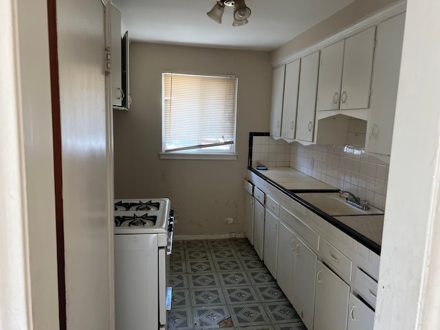 kitchen with tasteful backsplash, baseboards, white range with gas cooktop, a ceiling fan, and a sink