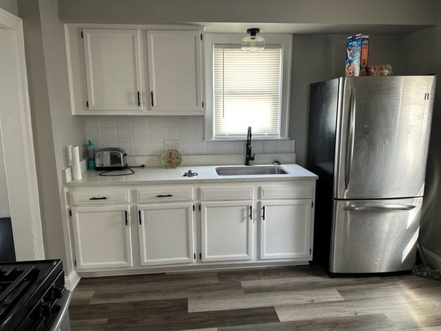 kitchen featuring wood finished floors, freestanding refrigerator, a sink, light countertops, and white cabinetry