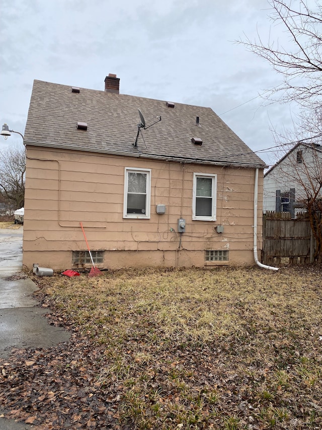 rear view of house with fence, a chimney, and a shingled roof