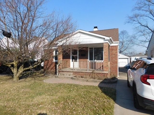 bungalow featuring an outbuilding, a porch, a chimney, a front lawn, and brick siding