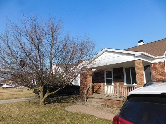 view of property exterior with a chimney, brick siding, a porch, and a lawn