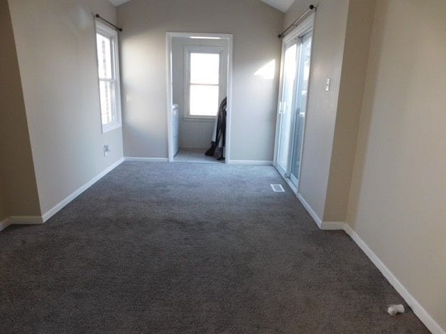 carpeted empty room with baseboards, lofted ceiling, and visible vents