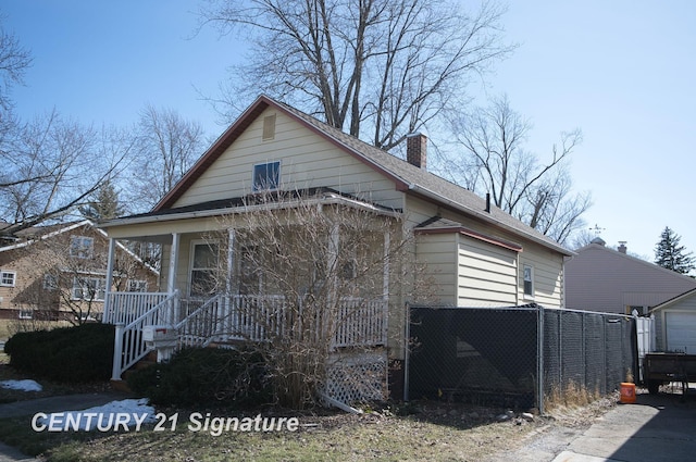 view of front of home with a shingled roof, an outbuilding, covered porch, and a chimney