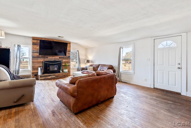 living area with a wealth of natural light, lofted ceiling, a fireplace, and hardwood / wood-style flooring