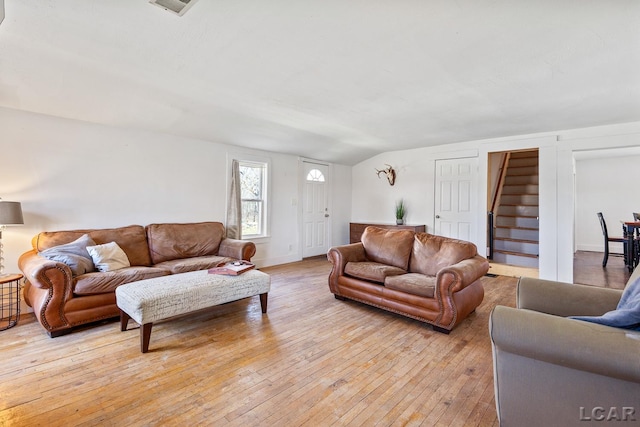 living room featuring light wood-style flooring, stairs, baseboards, and vaulted ceiling