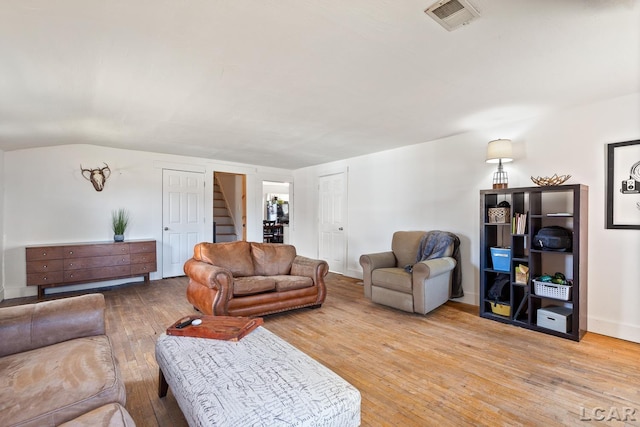 living room featuring visible vents, light wood-style flooring, stairs, and lofted ceiling