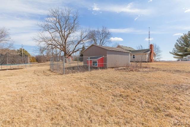 view of yard featuring an outdoor structure, a trampoline, fence, and an outbuilding