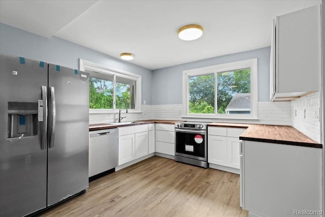 kitchen with a sink, stainless steel appliances, light wood-style flooring, and decorative backsplash