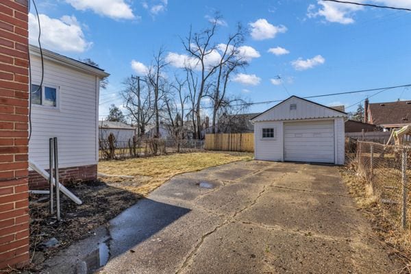 view of yard with an outbuilding, concrete driveway, a garage, and fence