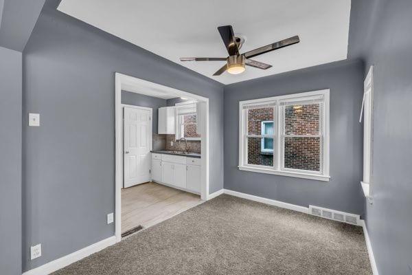 spare room featuring baseboards, a ceiling fan, visible vents, and light carpet