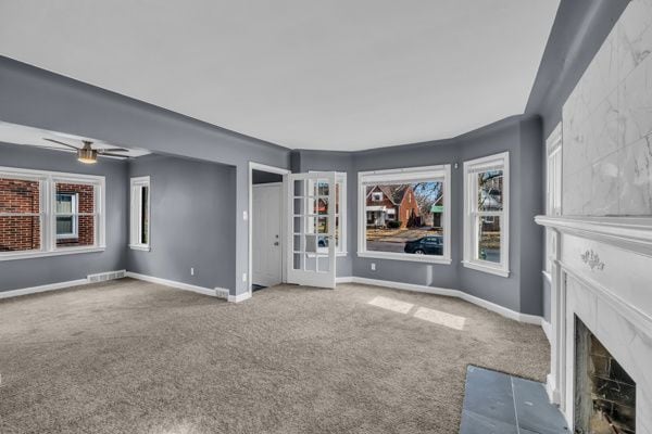 unfurnished living room featuring ceiling fan, carpet flooring, baseboards, and a premium fireplace