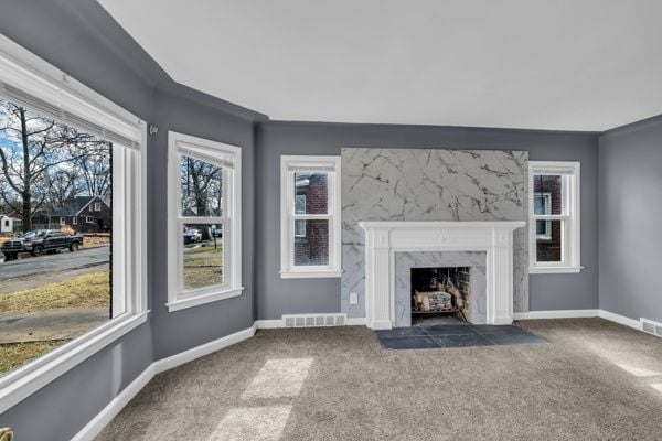 unfurnished living room with a high end fireplace, visible vents, baseboards, and carpet floors