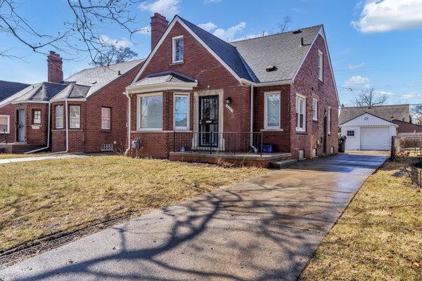 view of front of property with brick siding, a front lawn, a garage, an outdoor structure, and driveway