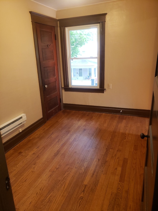 unfurnished room featuring baseboards, wood-type flooring, and a baseboard radiator