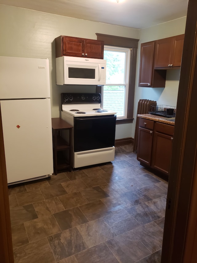 kitchen featuring baseboards, white appliances, and stone finish floor