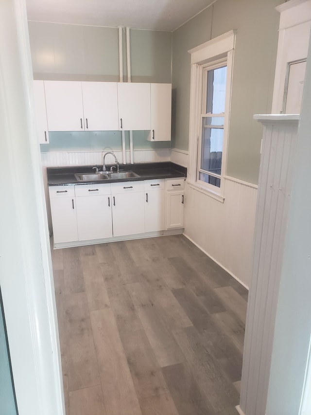 kitchen with dark countertops, white cabinets, light wood finished floors, and a sink