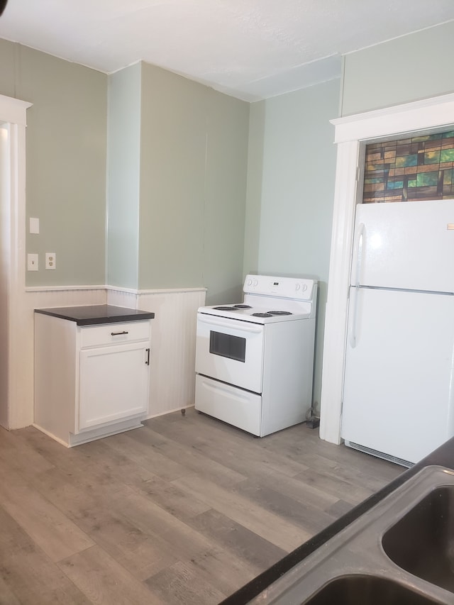 kitchen with white appliances, dark countertops, light wood-style flooring, and white cabinetry