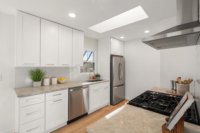 kitchen featuring a sink, stainless steel appliances, light wood-style floors, wall chimney range hood, and backsplash