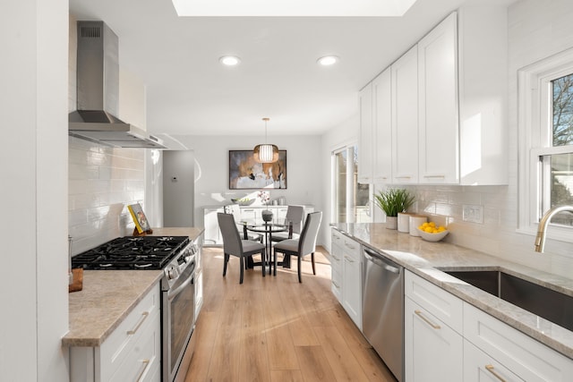 kitchen with a sink, wall chimney range hood, white cabinetry, stainless steel appliances, and light wood finished floors