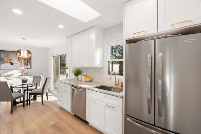 kitchen with light wood-style flooring, a sink, tasteful backsplash, appliances with stainless steel finishes, and white cabinets