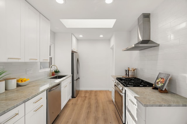 kitchen with a skylight, a sink, stainless steel appliances, light wood-style floors, and wall chimney exhaust hood