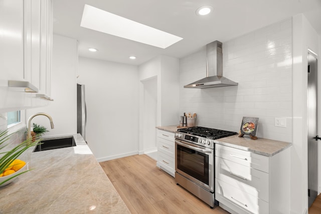 kitchen featuring light wood-style flooring, a sink, wall chimney range hood, decorative backsplash, and stainless steel gas range