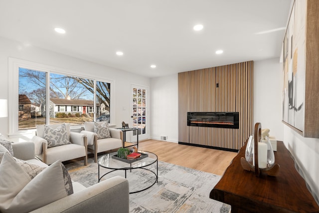 living room with recessed lighting, light wood-style flooring, visible vents, and a glass covered fireplace