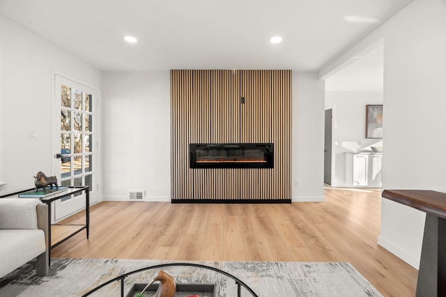 living area with visible vents, baseboards, recessed lighting, wood finished floors, and a glass covered fireplace