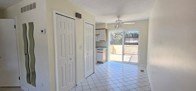 hallway with light tile patterned floors, baseboards, visible vents, and a textured ceiling